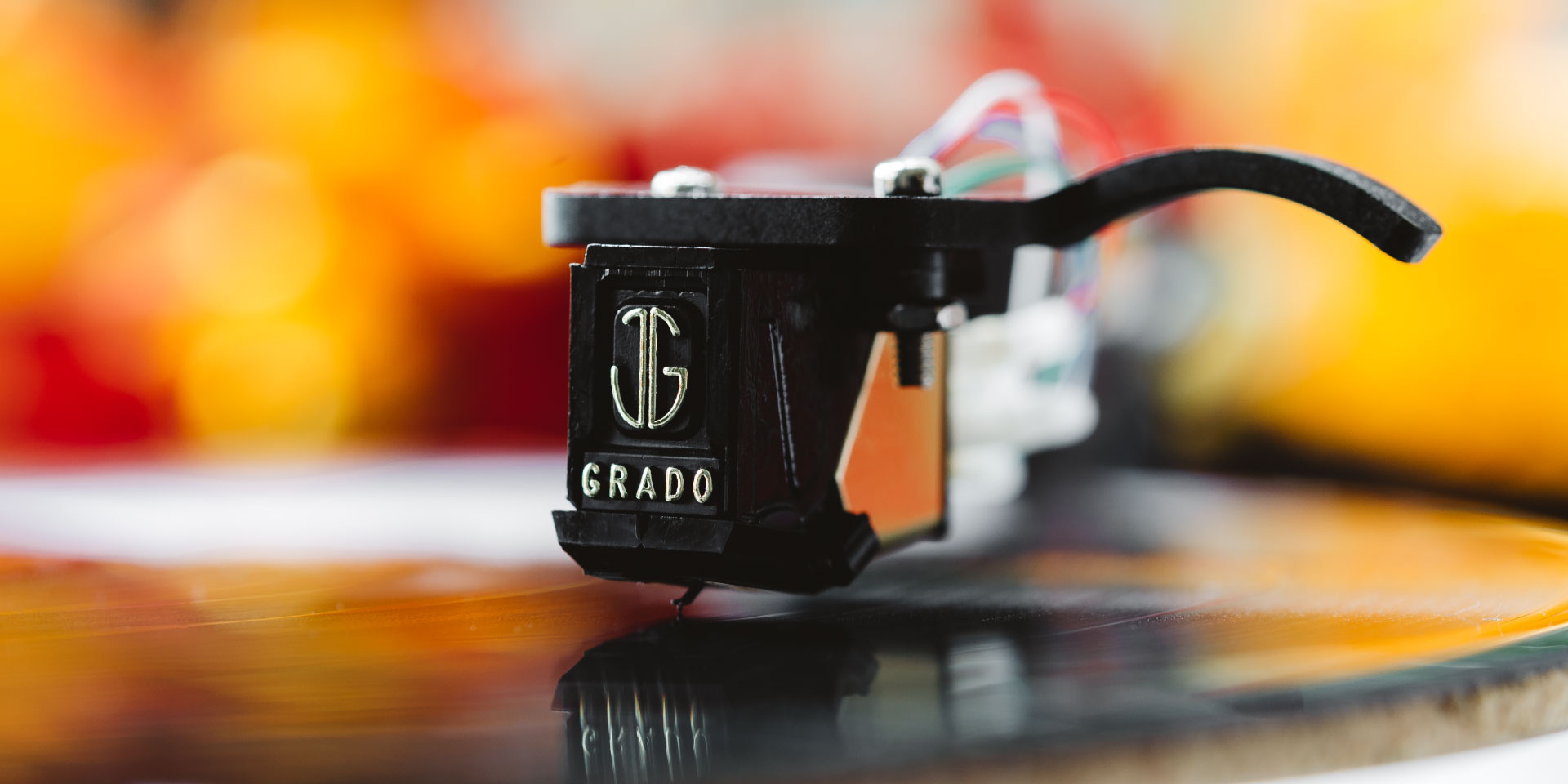 Photo of Grado Gold3 / Silver3 Phono Cartridge playing a record in front of a blurred orange background