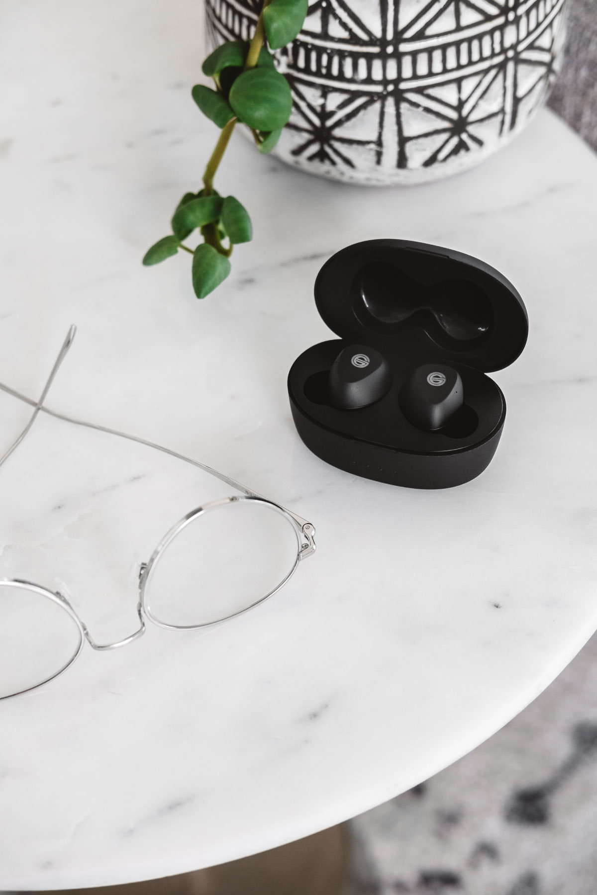 Photo of the GT220 headphones in their case on a white marble table next to a potted plant and glasses