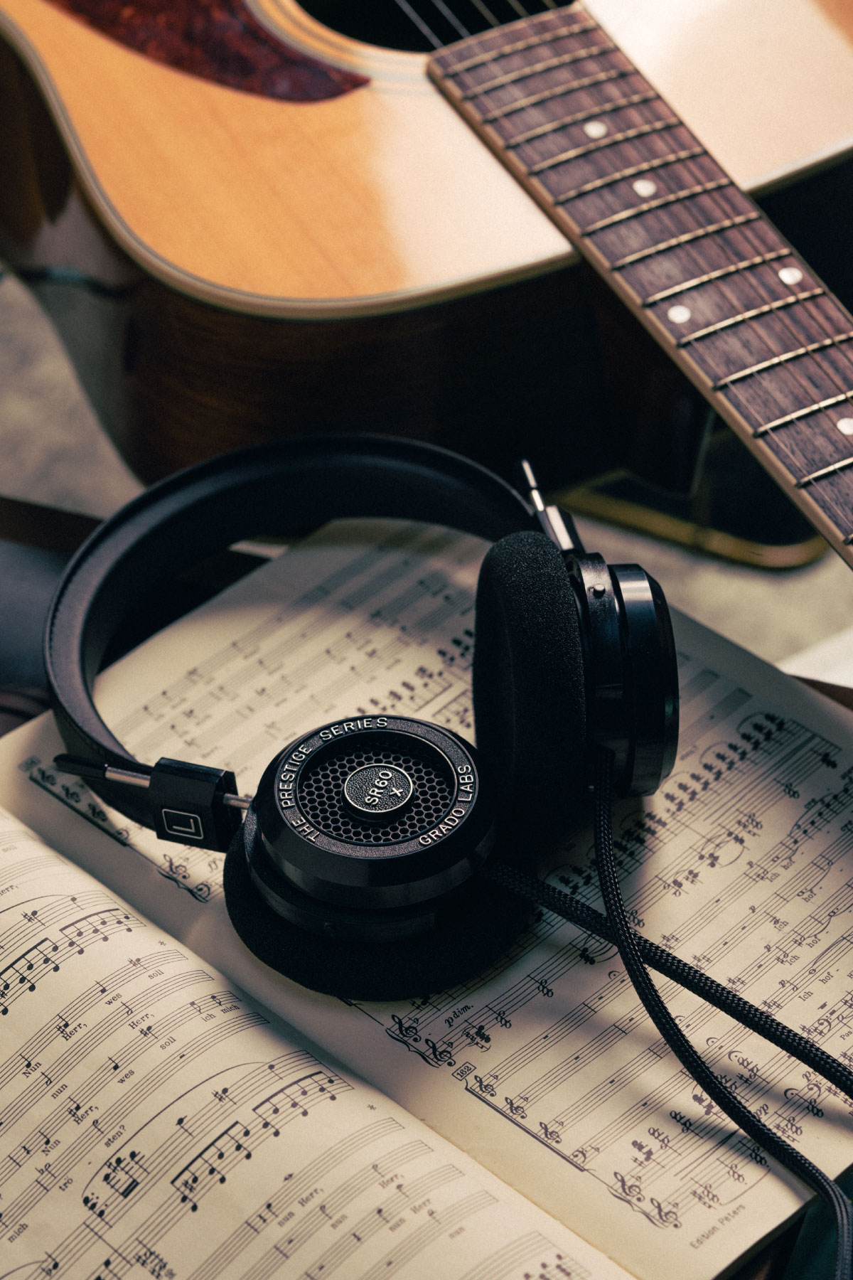 Photo of SR60x headphones resting on an open book of musical notations next to a guitar